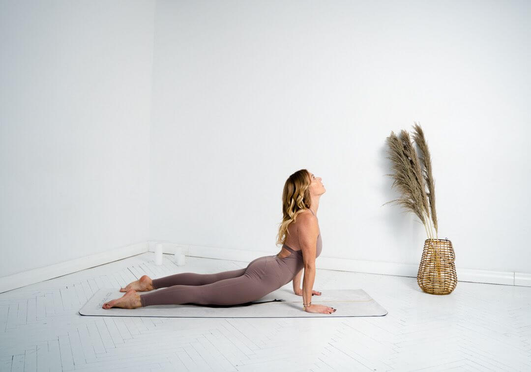 Iwona Michalska w pozycji psa skierowanego w górę (urdhva mukha svanasana) na macie, w jasnej przestrzeni z pampasami.